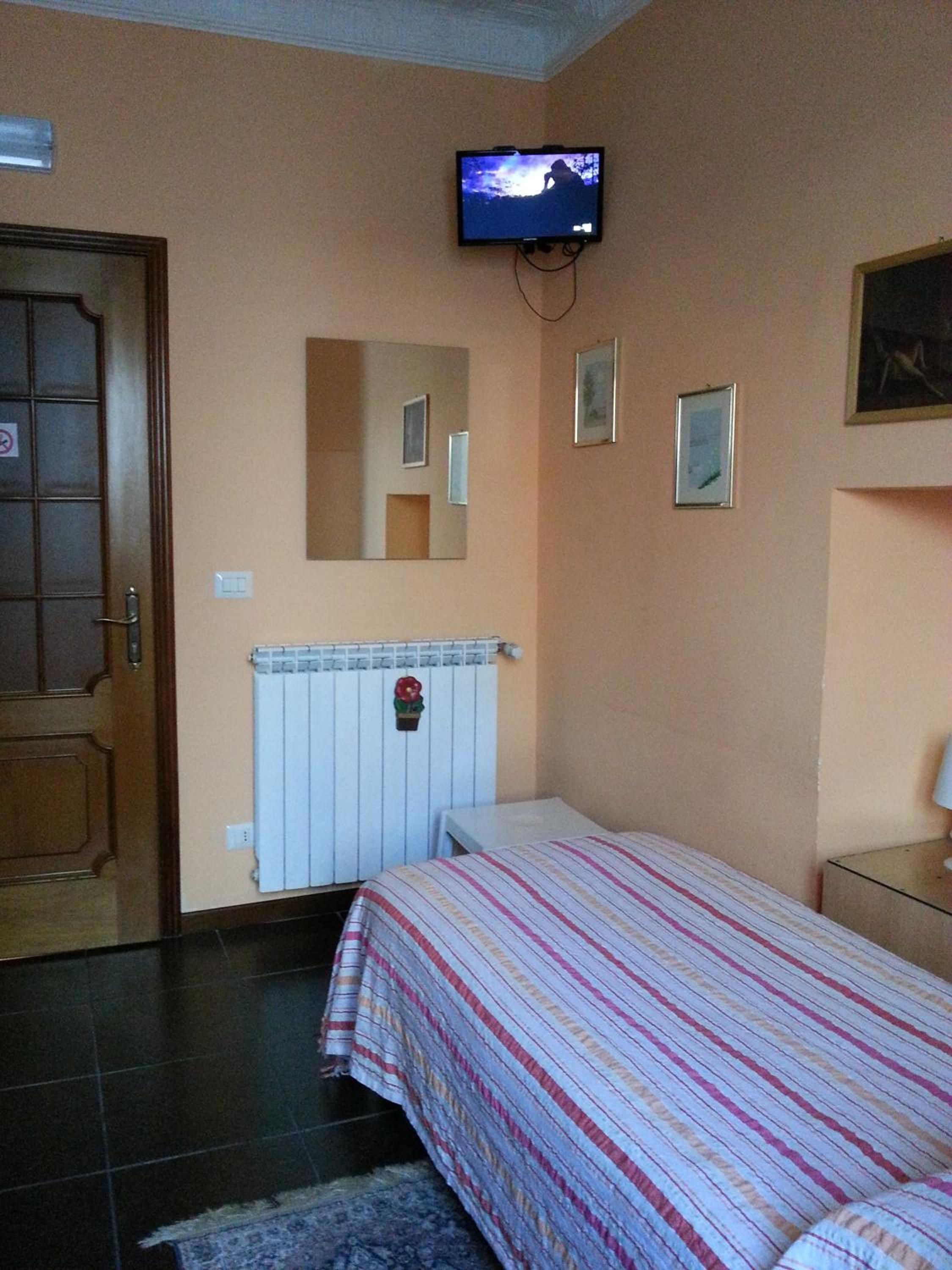 A bedroom with a bed, a television mounted on the wall, a radiator, and a door with a sign.