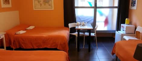 Habitación de hotel con dos camas, una mesita con sillas, una ventana y un televisor.