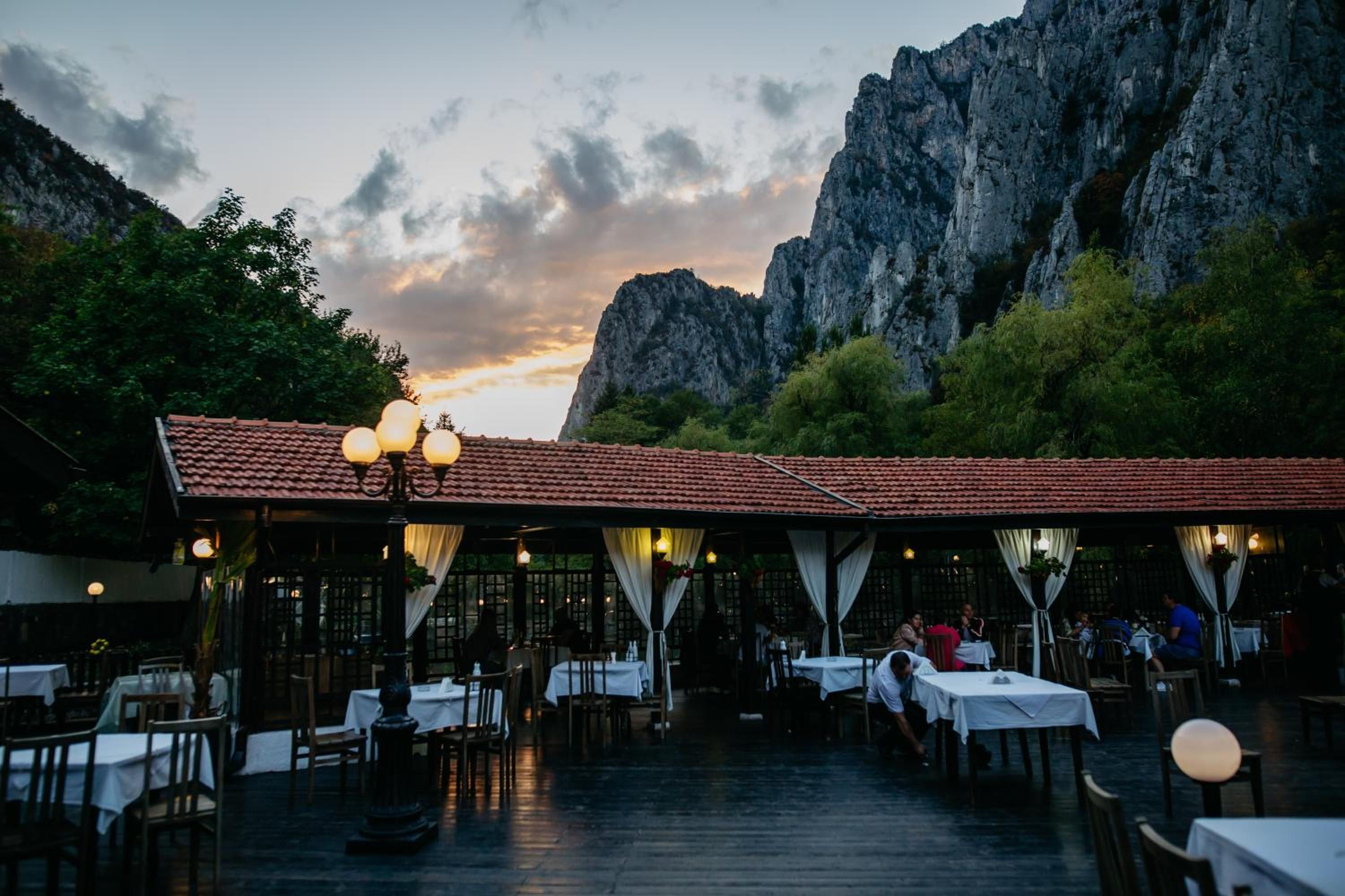 An outdoor restaurant with tables and chairs, set against a backdrop of a mountainous landscape.
