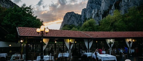 Un restaurante al aire libre con mesas y sillas, con un paisaje montañoso de fondo.