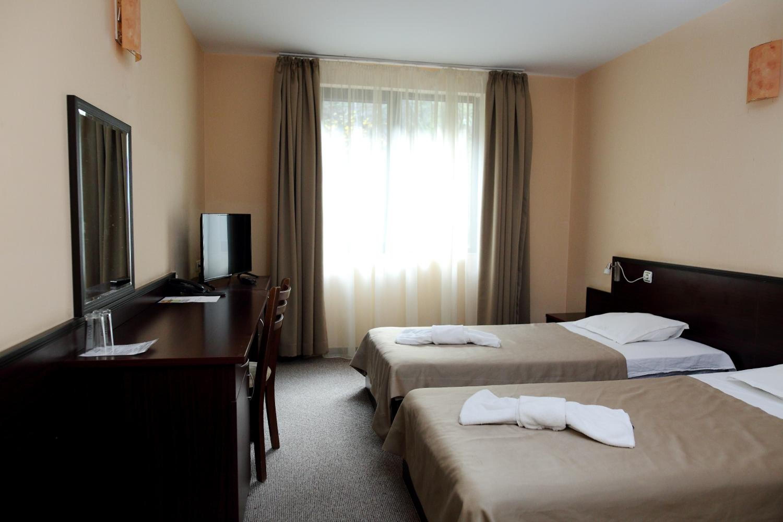 A hotel room with two beds, a desk, a television, and a window with curtains.