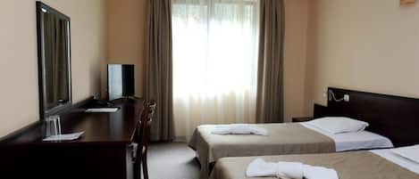Habitación de hotel con dos camas, un escritorio, un televisor y una ventana con cortinas.