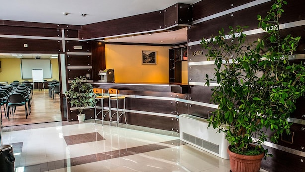 Een hotel lobby met een receptiebalie, een zithoek en een grote kamerplant.
