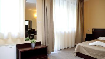 A hotel room with a bed, a desk with a chair, a mirror, and a potted plant.