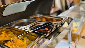 Disposição de buffet com vários recipientes de comida, incluindo ovos mexidos e salsichas.