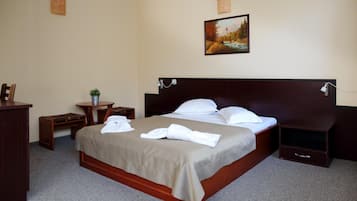Een hotelkamer met een groot bed, nachtkastje, bureau, stoel, een kleine potplant en een schilderij aan de muur.