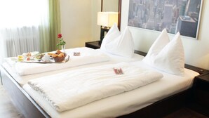 Hotelkamer met een bed, kussens, een nachtkastje, een lamp, een raam met uitzicht over de stad, en een ontbijtplateau op het bed.