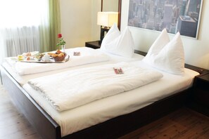 A hotel room with a bed, pillows, a nightstand, a lamp, a window with a city view, and a breakfast tray on the bed. - Stadthotel Restaurant Auerhahn (Voecklabruck)