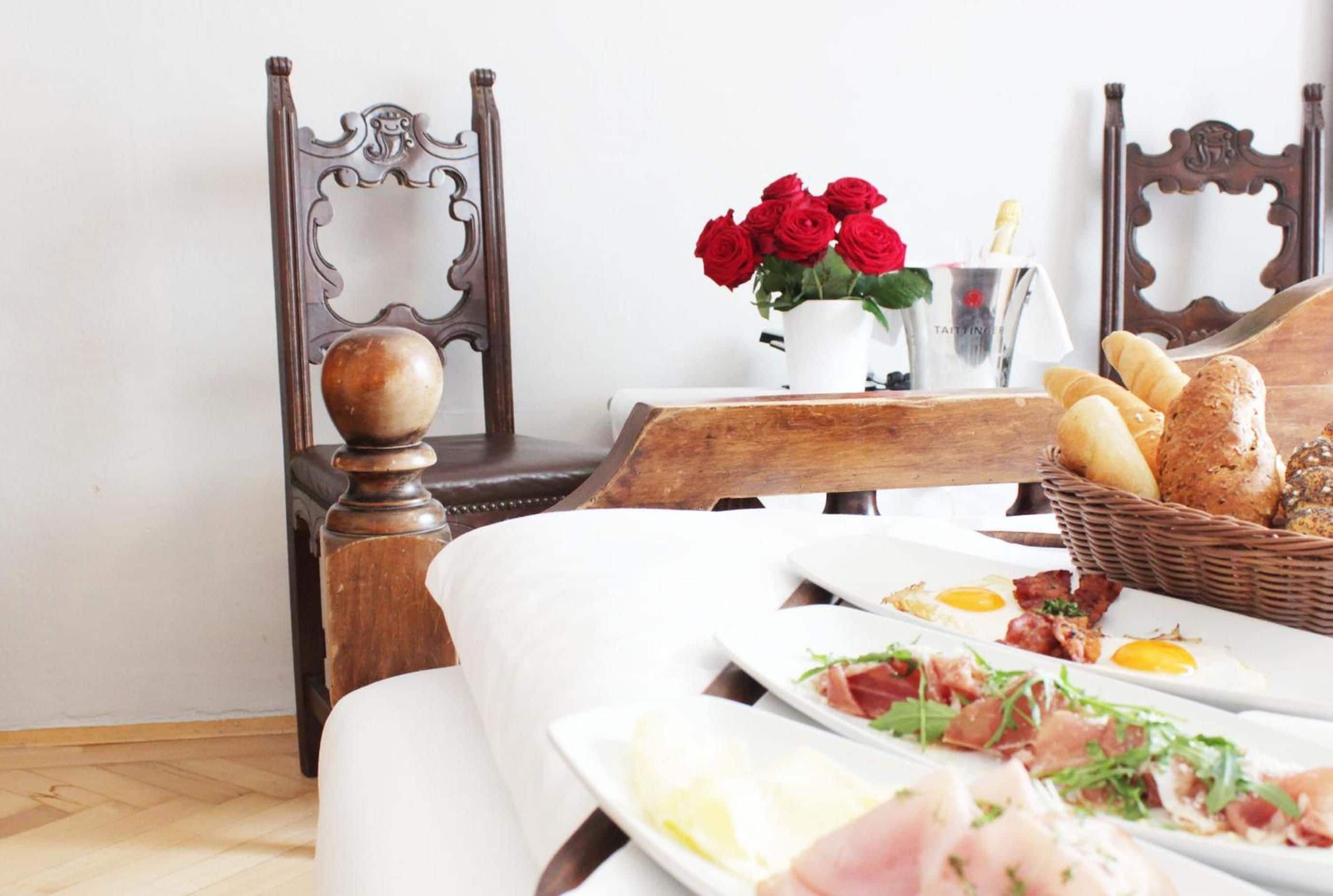 A neatly arranged breakfast table with plates of food, a vase of red roses, and a basket of bread.
