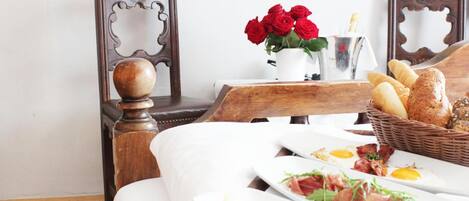 A neatly arranged breakfast table with plates of food, a vase of red roses, and a basket of bread.
