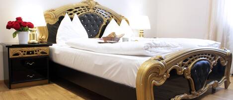 A bed with a black and gold frame, white bedding, and a nightstand with drawers and a vase of red roses.