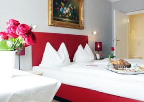 A hotel room with a bed, pillows, a vase of red roses, a painting, and a breakfast tray. - Stadthotel Restaurant Auerhahn (Voecklabruck)