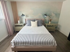 A bedroom with a bed, two bedside tables, a nightstand, a window with curtains, and a wall with a textured finish. - Sarasota Private Getaway Paradise (Sarasota)