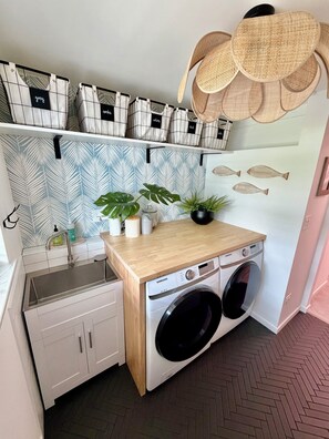 A compact kitchen with a washing machine, a sink, and a countertop with potted plants. - Sarasota Private Gateway Paradise (Sarasota)