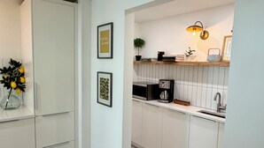 Ett modernt kök med vita skåp, en inbyggd mikrovågsugn och en bänkskiva med en kaffebryggare.