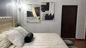 A bedroom with a bed, a headboard, two abstract paintings, a door, and a wall-mounted light fixture. -      Casa Vacacional para 10 
Alberca Privada  Cerca de la Playa (South Padre Island)