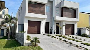 A modern two-story residential building with a garage, a driveway, and a well-maintained lawn. -      Casa Vacacional para 10 
Alberca Privada  Cerca de la Playa (South Padre Island)