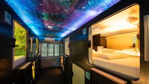 Un vagón de tren con techo decorado con motivos galácticos, una cama con vistas y un ventanal a un paisaje natural.