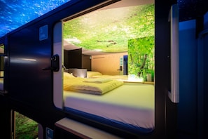 A train compartment with a bed, a small table, and a window with a view of greenery. - Capsule Hotel - Lucerne Thelab (Lucerne)