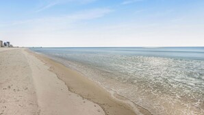 Ein Strand mit klarem Wasser, sandigem Ufer und einem entfernten Steg.