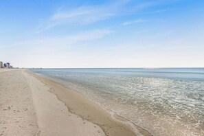 Ein Strand mit klarem Wasser, sandigem Ufer und einem entfernten Steg.