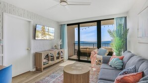 Ein Wohnzimmer mit Sofa, Couchtisch, Fernseher, Schrank und Meerblick durch große Fenster.