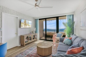 Ein Wohnzimmer mit Sofa, Couchtisch, Fernseher, Schrank und Meerblick durch große Fenster.