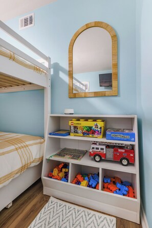 A child's bedroom with bunk beds, a bookshelf with toys, and a mirror. - Beach Condo Loved for Location & Thoughtful Extras (Gulf Shores)