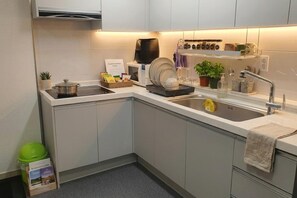 A modern kitchen with a built-in microwave, a kettle, and a dish rack. - Ara Guesthouse (Busan)