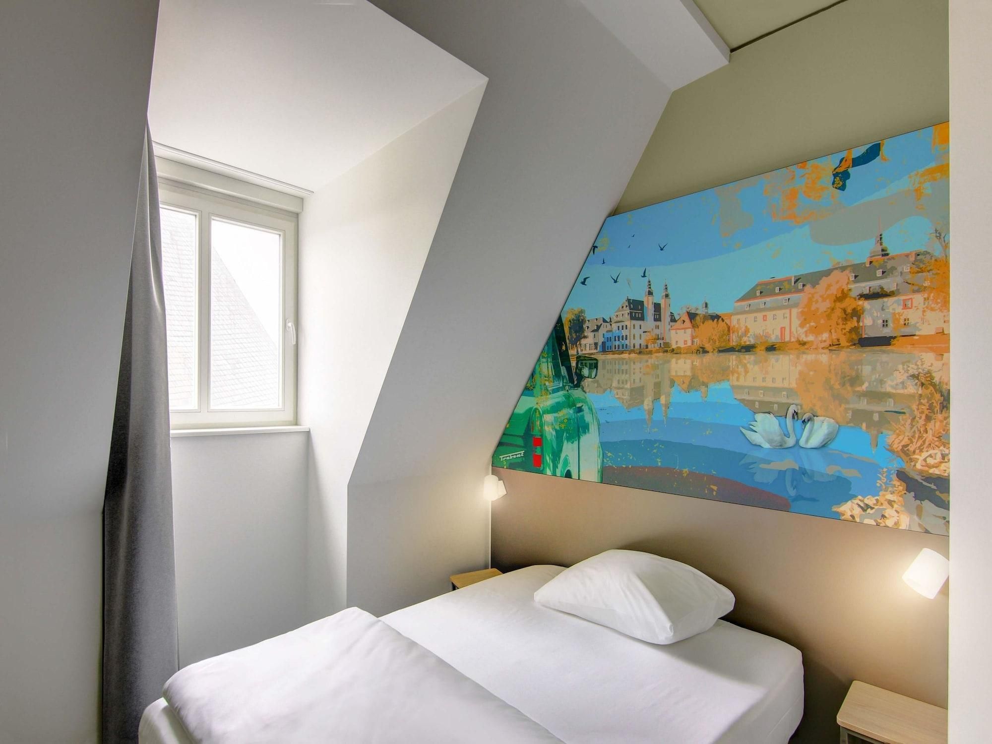 A bedroom with a bed, a window, and a cityscape painting on the wall.