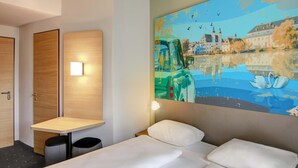 A hotel room with a bed, a small table, a trash bin, and a wall-mounted light. - B&B Hotel Zwickau (Zwickau)