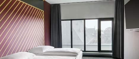 A hotel room with a bed, a large window, and a view of buildings.
