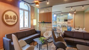 A hotel lobby with a B&B sign, seating arrangements, and a view of the dining area. - B&B Hotel Zwickau (Zwickau)