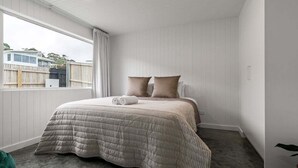 A bedroom with a bed, pillows, a window, and a view of a house outside. - White Pebble - Bicheno Accommodation (Bicheno)