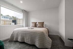 Ein Schlafzimmer mit einem Bett, Kissen, einem Fenster und Blick auf ein Haus.