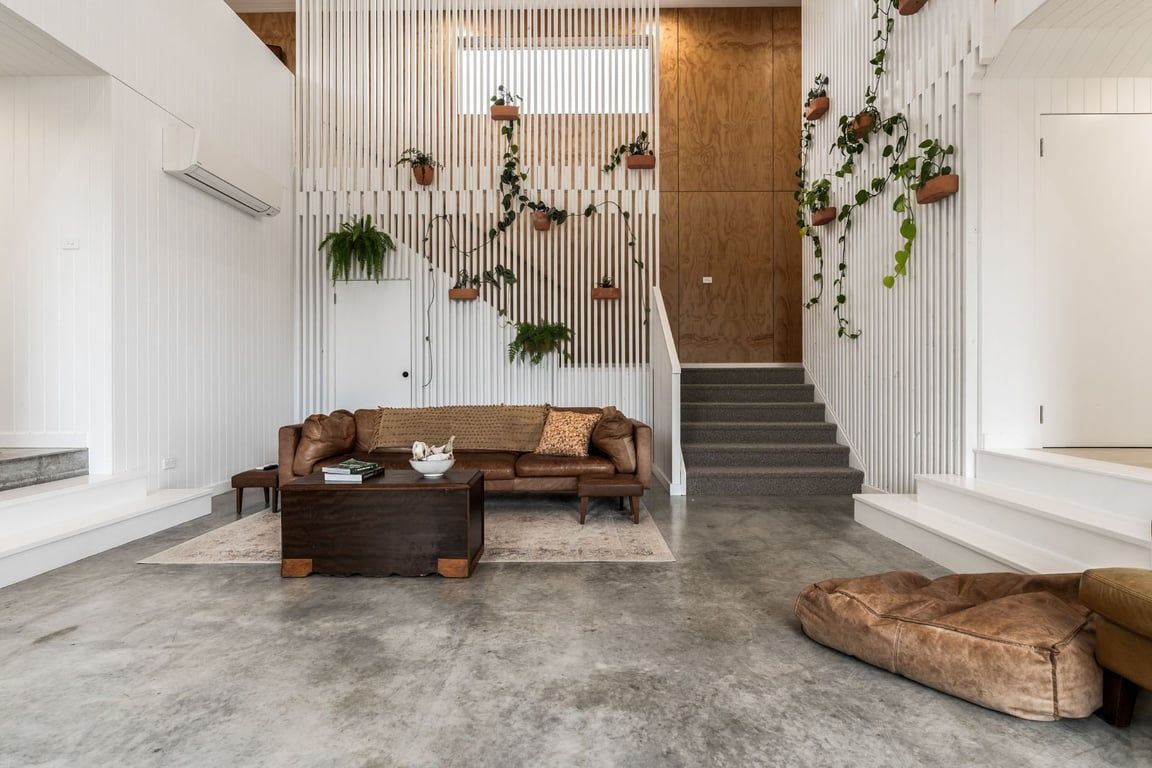 Un salon moderne avec un canapé, une table basse et un panier pour chien. On y trouve un escalier avec des marches en bois et un mur blanc orné de lattes verticales.