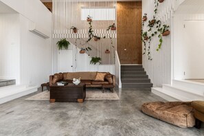 A modern living room with a sofa, coffee table, and a dog bed. There is a staircase with a wooden finish and a white wall with vertical slats. - White Pebble - Bicheno Accommodation (Bicheno)