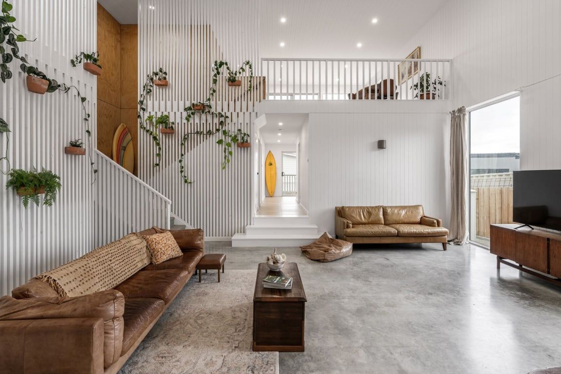 A spacious living area with a high ceiling, a staircase leading to an upper level, and a large window providing a view.