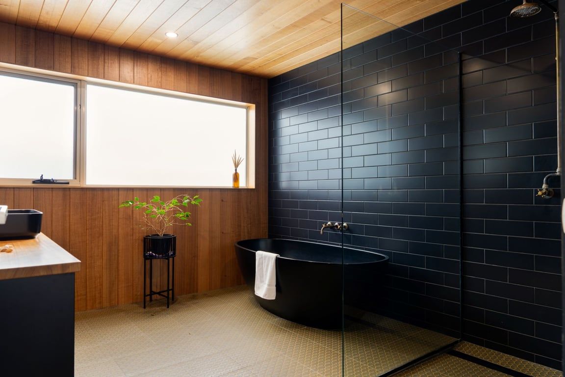 A modern bathroom with a black bathtub, wooden paneling, and a large window.