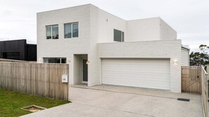 A modern two-story residential building with a garage, a wooden fence, and a well-maintained lawn. - White Pebble - Bicheno Accommodation (Bicheno)
