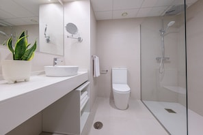 A modern bathroom with a white sink, mirror, toilet, and glass shower enclosure. - Aduana Suites (Salou)