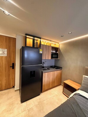 A compact kitchenette with a refrigerator, microwave, and wooden cabinets. - Luxury Loft Jacuzzi, Gym and Steam Bath Laureles (Medellín)