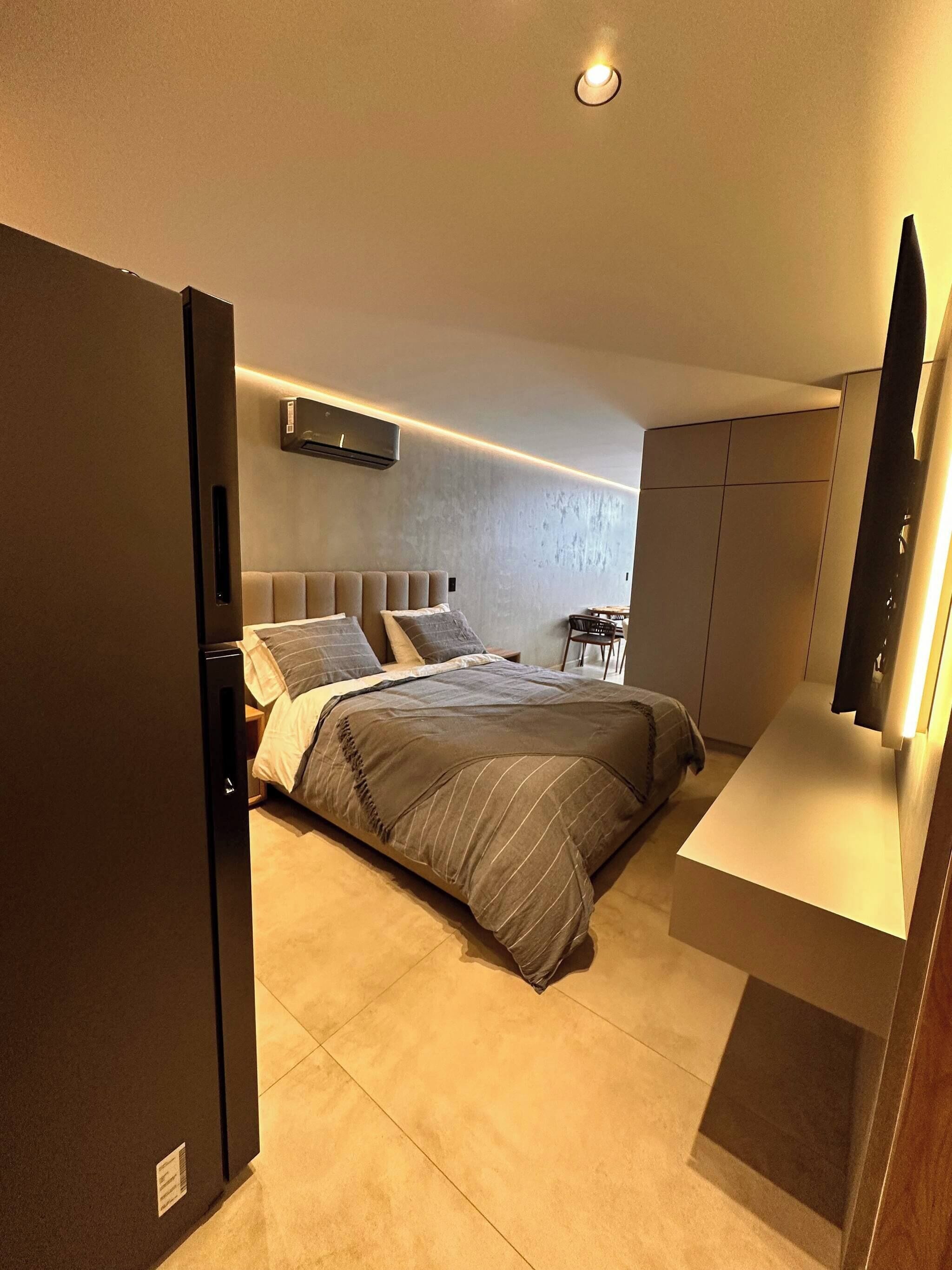 A modern bedroom with a bed, bedside tables, a built-in TV, and a wardrobe.