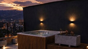 En tagterrasse med jacuzzi, siddeområde og to glas rødvin på et bord.