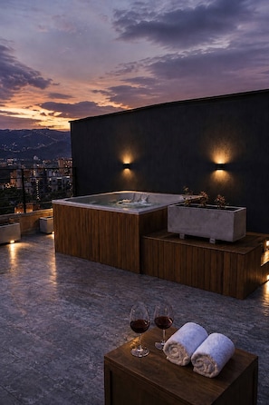 Eine Dachterrasse mit Whirlpool, Sitzgelegenheit und zwei Gläsern Rotwein auf einem Tisch.