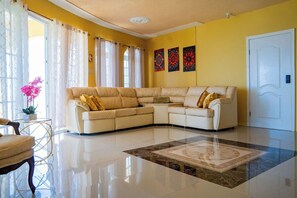 Una sala de estar con un sofá seccional color beige, una mesa de centro de vidrio y un tapete estampado.