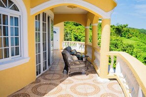 Ein Balkon mit Korbmöbeln, einem Tisch, einer Tür und Blick auf üppiges Grün.