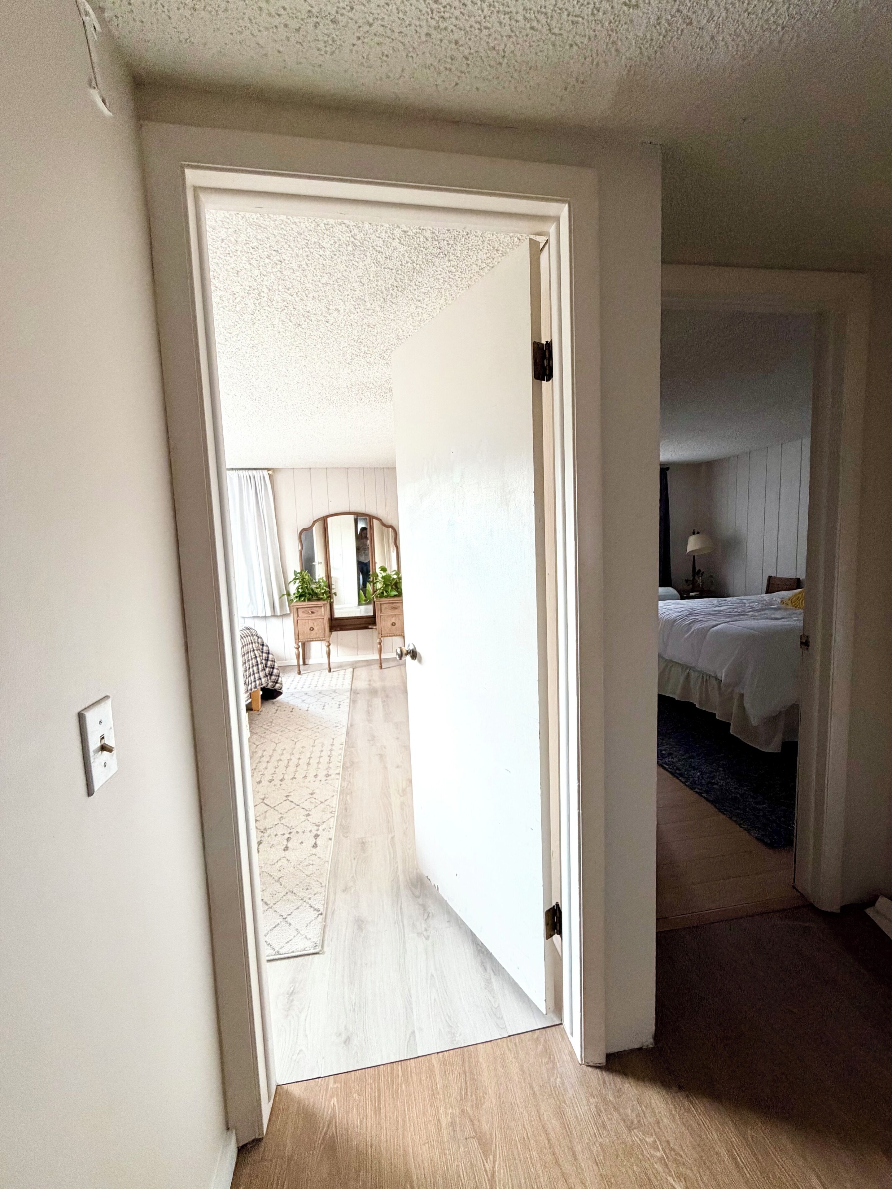 An open doorway leading to a room with a bed and a nightstand, a wooden floor, and a white ceiling.