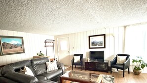 A living room with a leather sofa, two armchairs, a coffee table, a TV stand, and a potted plant. - Charming Apartment in Downtown Lyons! 3bed/2bath (Lyons)