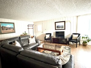 Ein Wohnzimmer mit einer Ledersofa, zwei Sesseln, einem Couchtisch, einer TV-Konsole und einer Topfpflanze.
